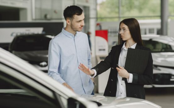 A salesperson and customer discussing car features in a dealership setting.
