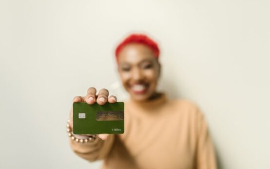 An African American woman smiling while holding out a green credit card.