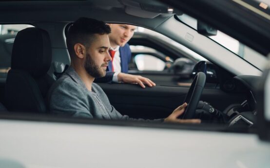 Man examining car interior with salesman at a dealership, highlighting car features.