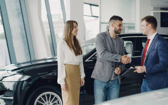 Customers shaking hands with dealer in showroom, sealing car purchase deal.
