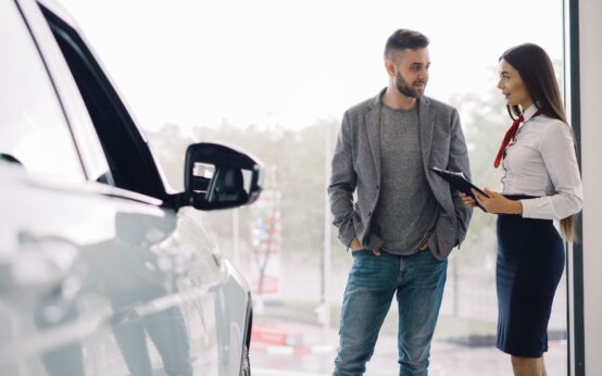 Man consulting with car salesperson in a showroom, discussing car options.